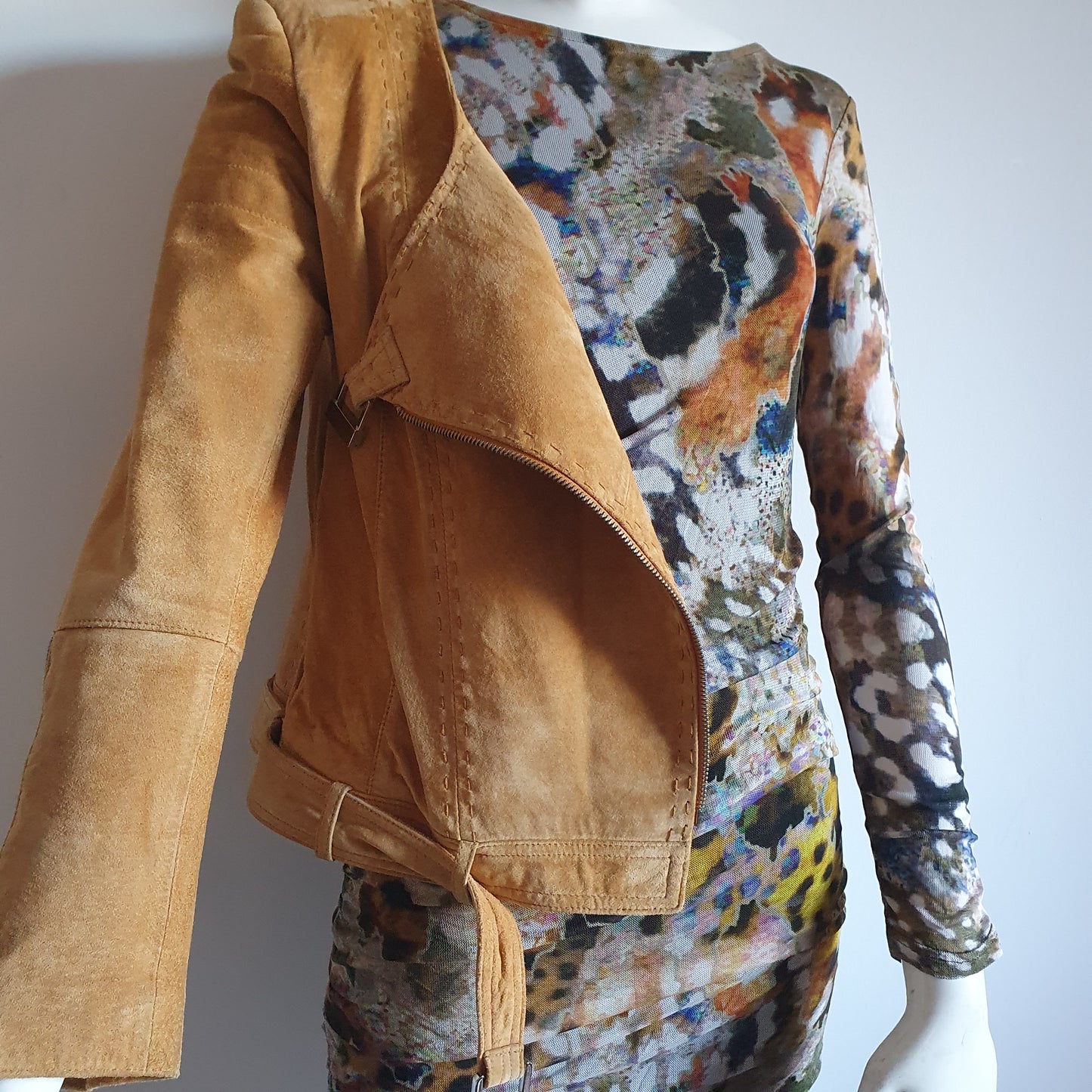 Veste en daim moutarde dépareillée sur robe imprimé artistique — vue de trois quarts, zip ouvert, détail texture cuir suédé
