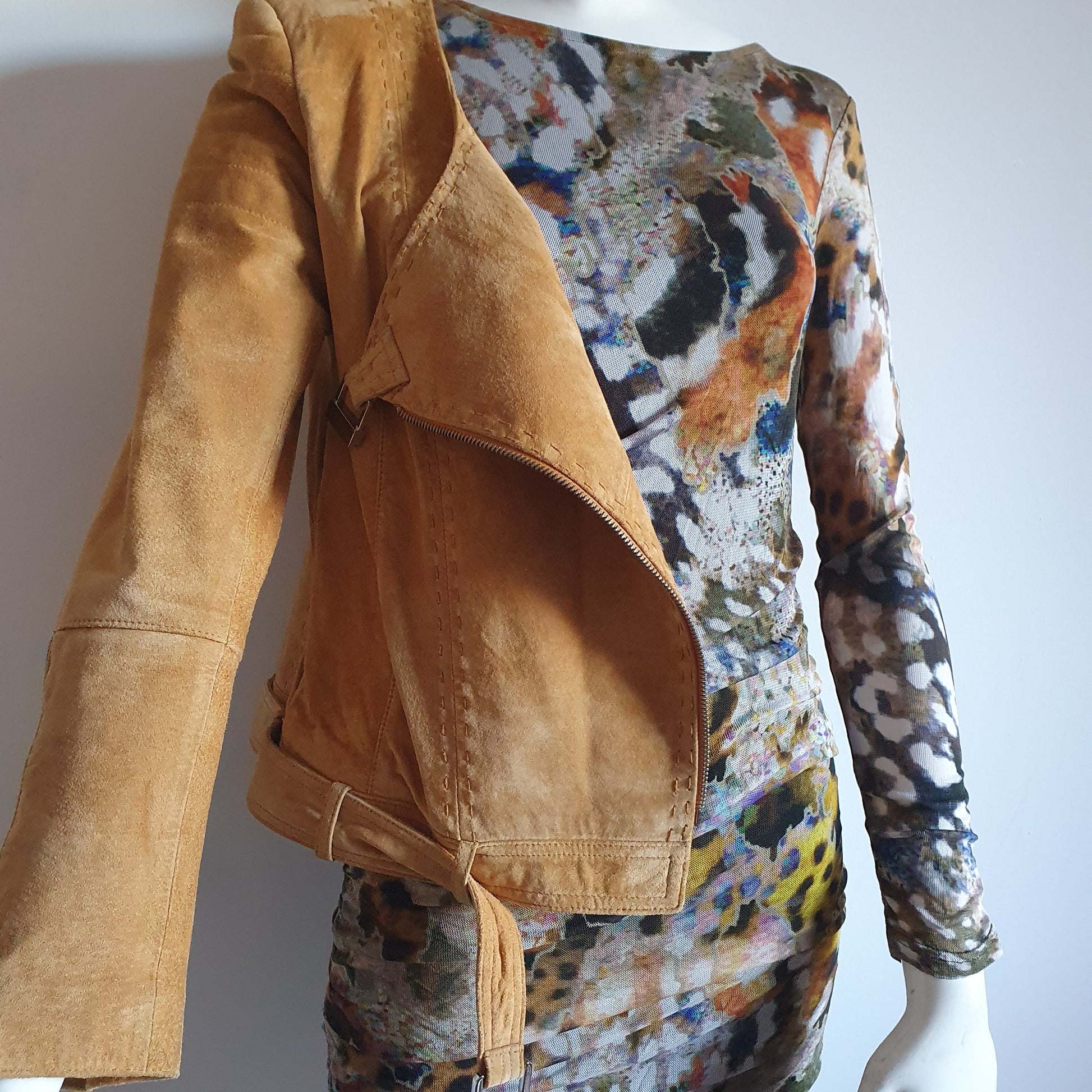 Veste en daim moutarde dépareillée sur robe imprimé artistique — vue de trois quarts, zip ouvert, détail texture cuir suédé