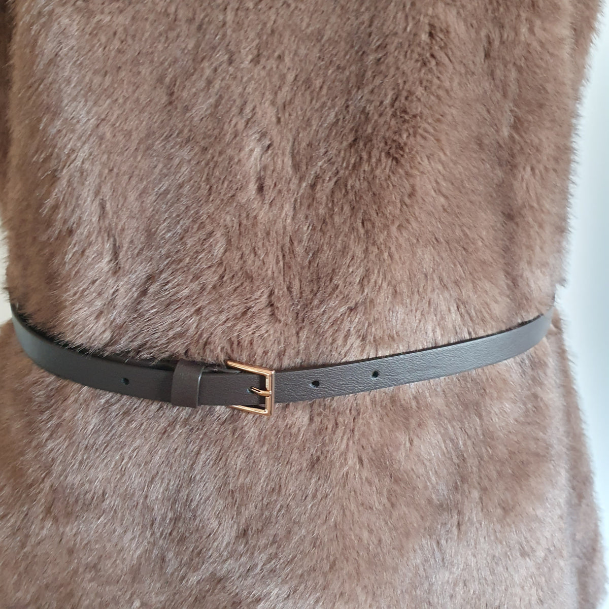 Détail de la fine ceinture sombre à boucle dorée sur la tunique en fausse fourrure taupe