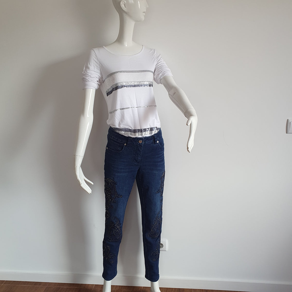 Jean bleu à arabesques et strass Madeleine associé à un haut blanc à bandes argentées sur mannequin.