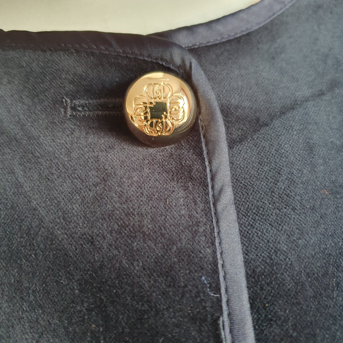 Bouton doré à motif en relief et bordure satinée sur le velours fin bleu nuit
