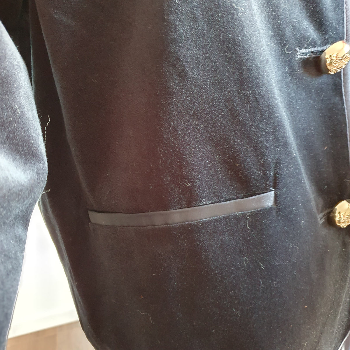 Détail de la bordure satinée d’une poche de la veste en velours bleu nuit 