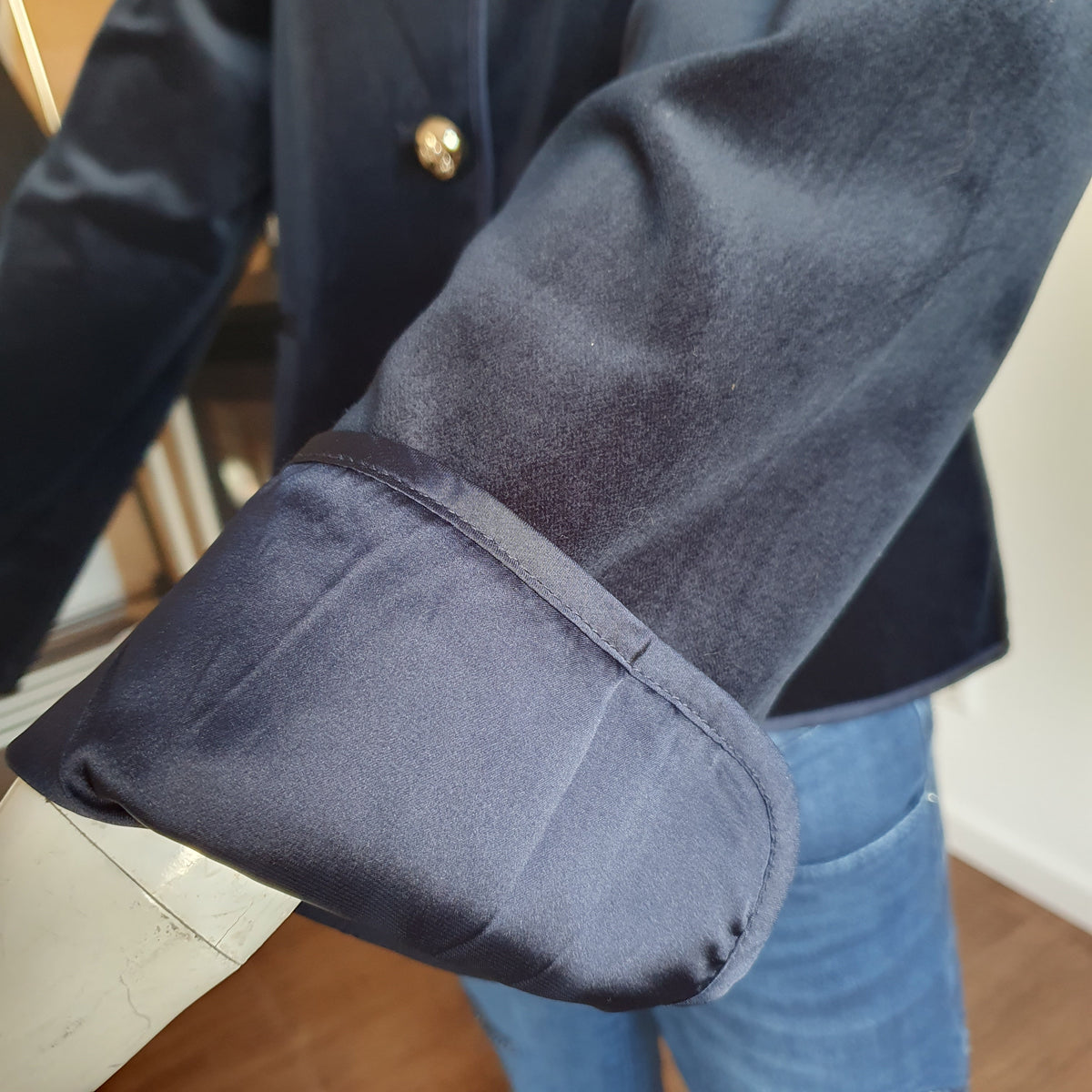 Gros plan du poignet retourné et de sa finition satinée sur la veste en velours bleu nuit 