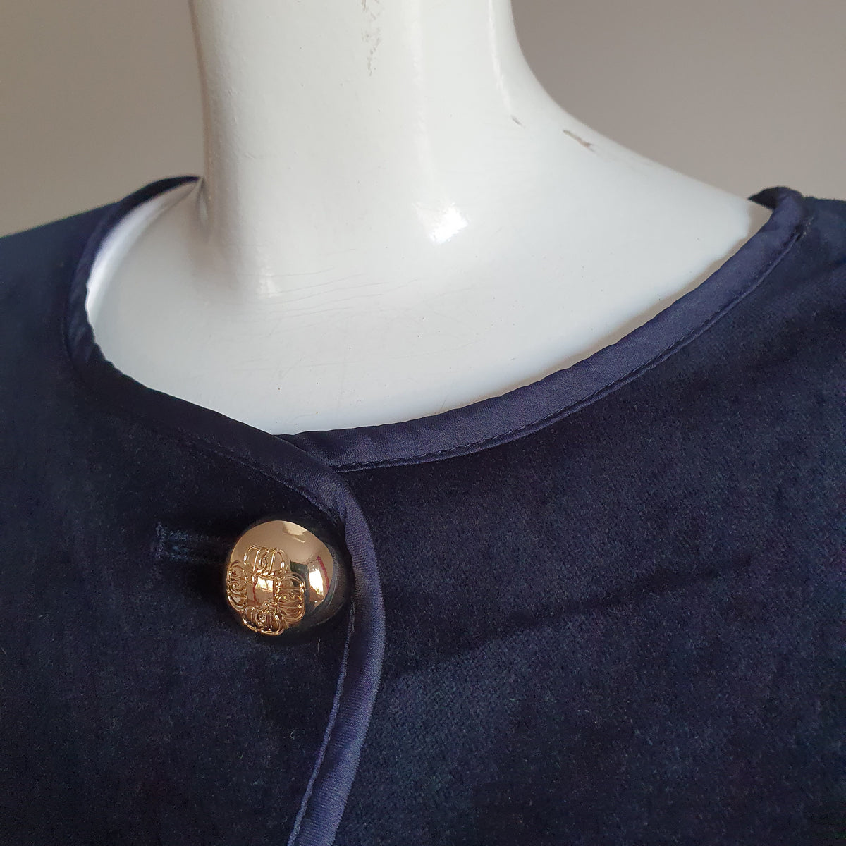 Encolure ronde bordée de satin et bouton doré en relief de la veste en velours bleu nuit