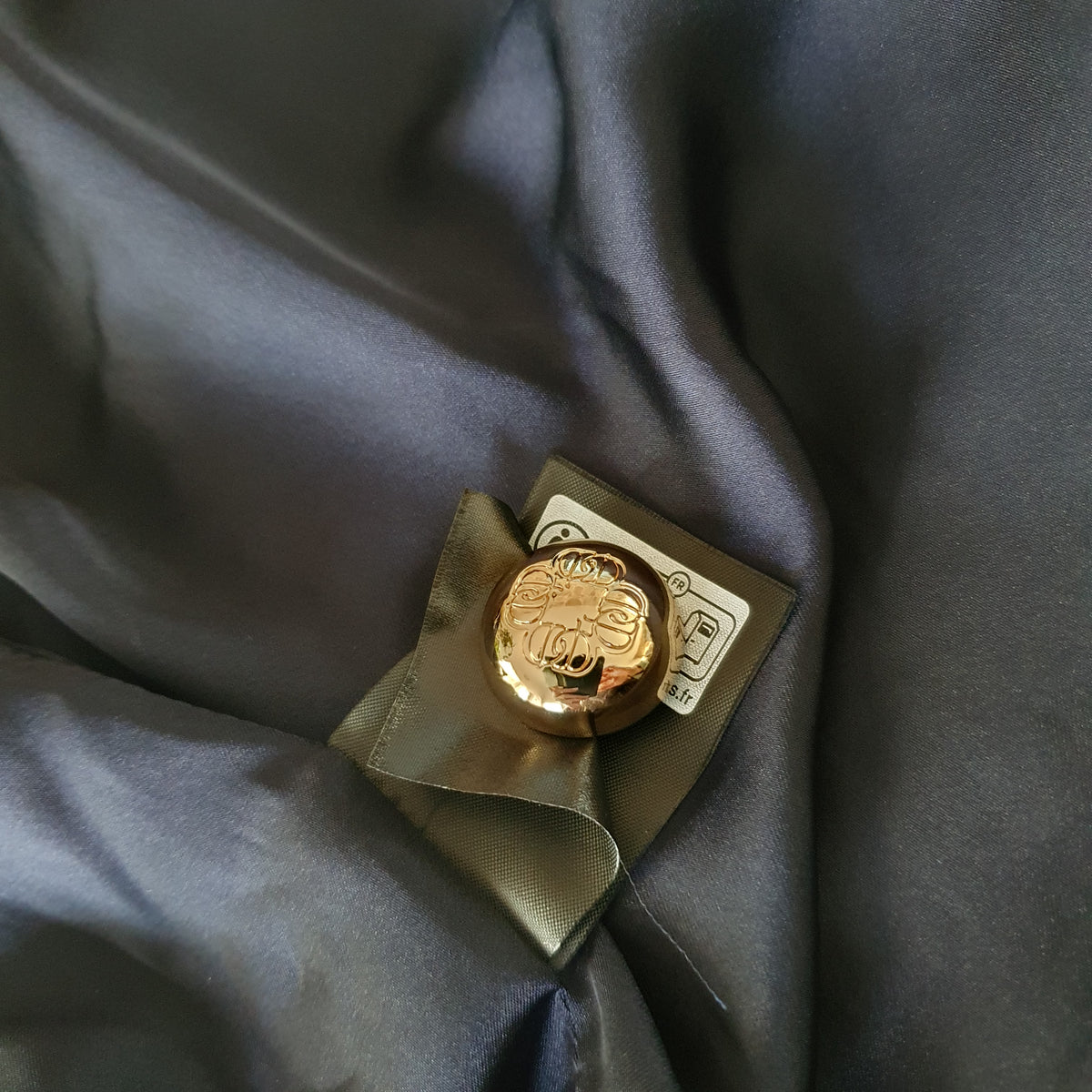 Bouton doré de rechange fixé à l’intérieur de la veste sur la doublure bleu nuit