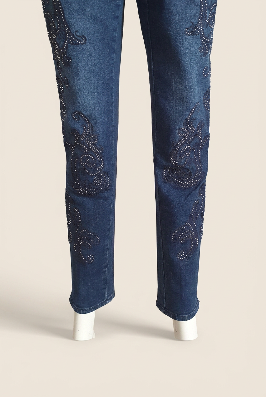  Bas des jambes du jean Madeleine : motifs arabesques à strass et ourlets, vue de face sur fond beige clair. 